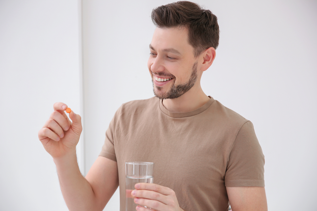 a man holding a glass of water and NMN pills