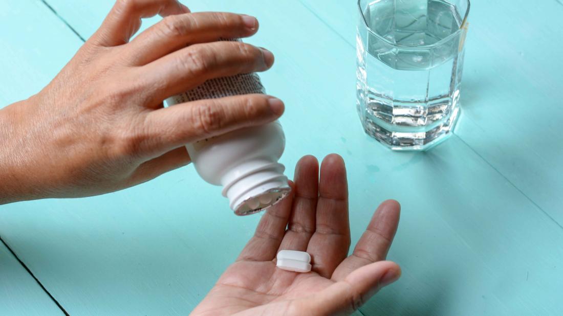 A picture of a person’s hand with two pills and a half-filled glass of water