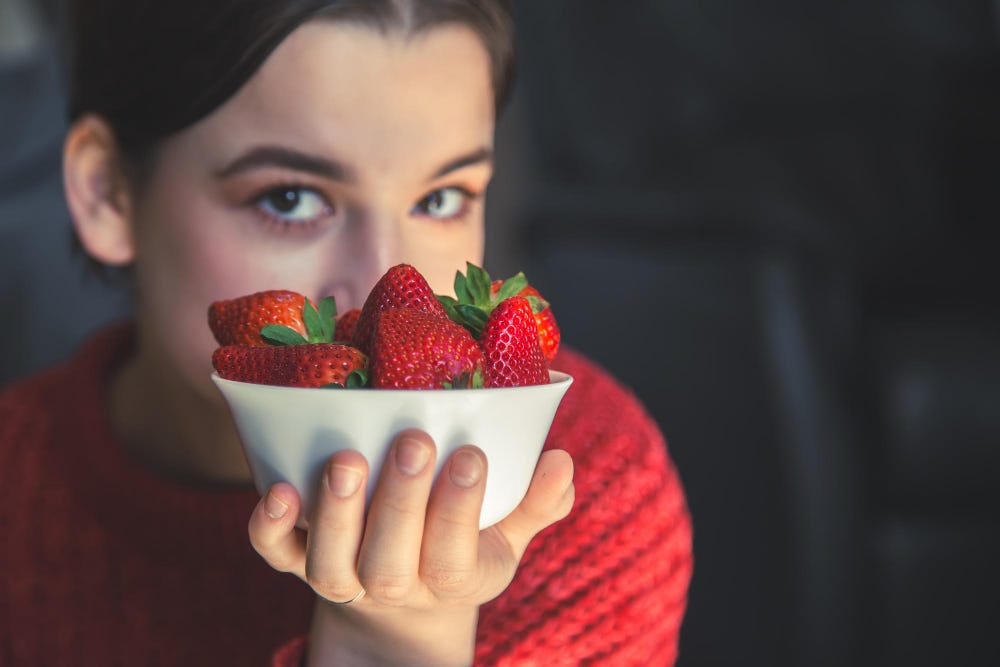A woman holding a bowl filled with strawberries