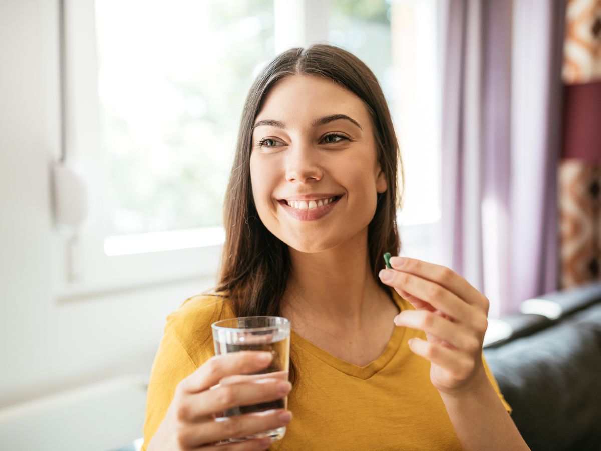a woman holding a glass of water and resveratrol pill